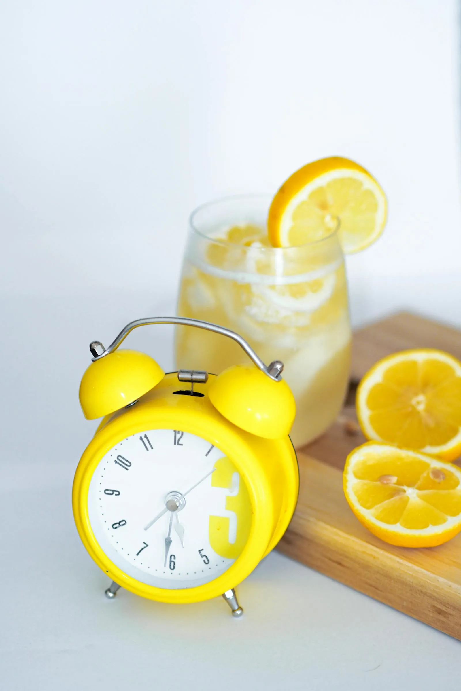 Yellow alarm clock beside a lemon drink on wood surface — a cue for scheduled eating