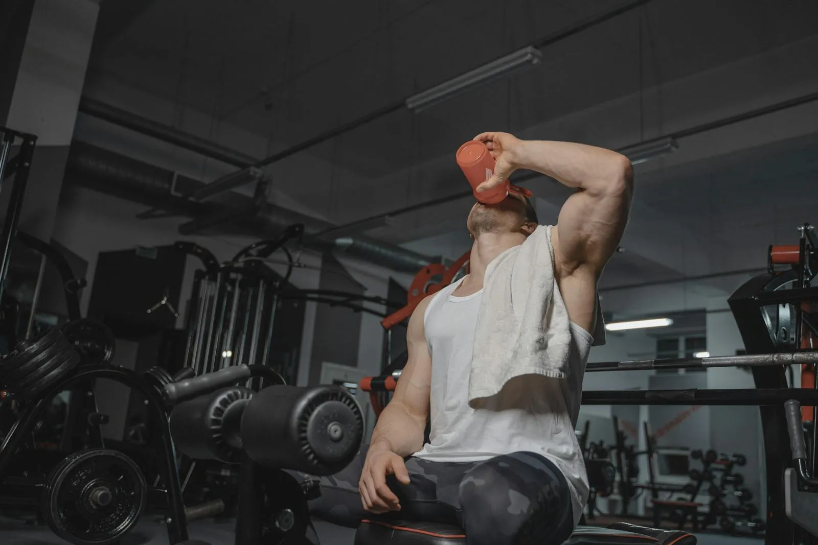 An athletic man drinks from a protein shaker bottle post-workout in a gym