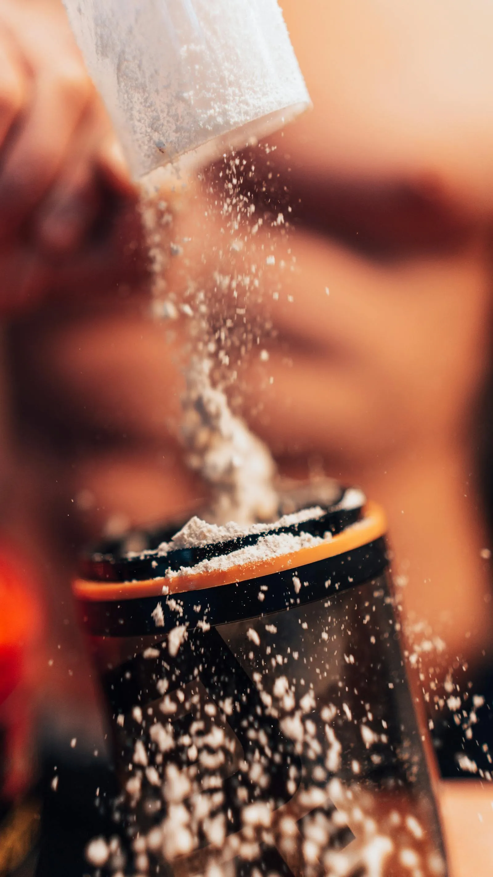 Protein powder being scooped into a blender shaker bottle with gym equipment nearby
