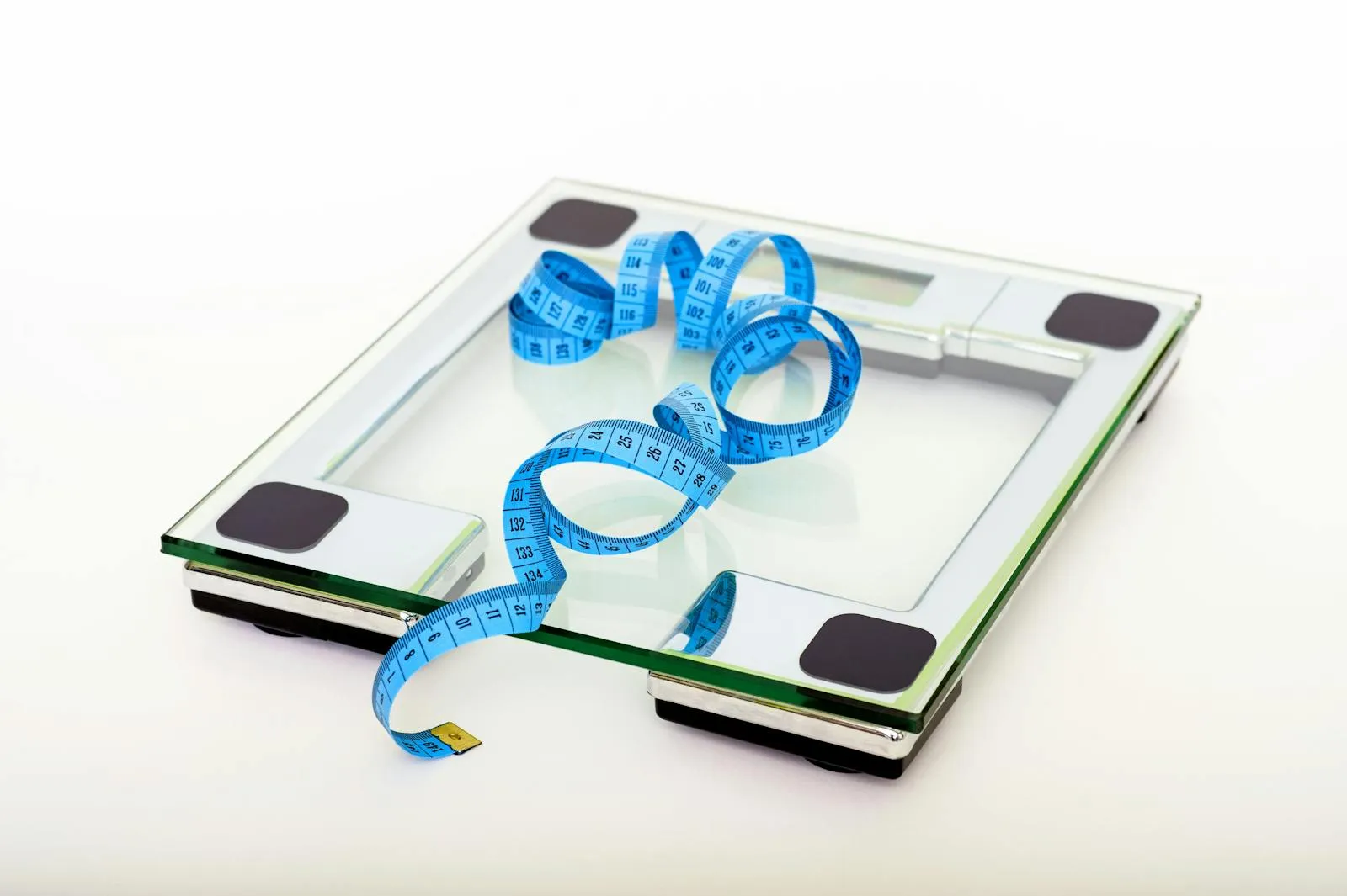 A digital glass bathroom scale with a blue measuring tape — the basic tools of weight tracking
