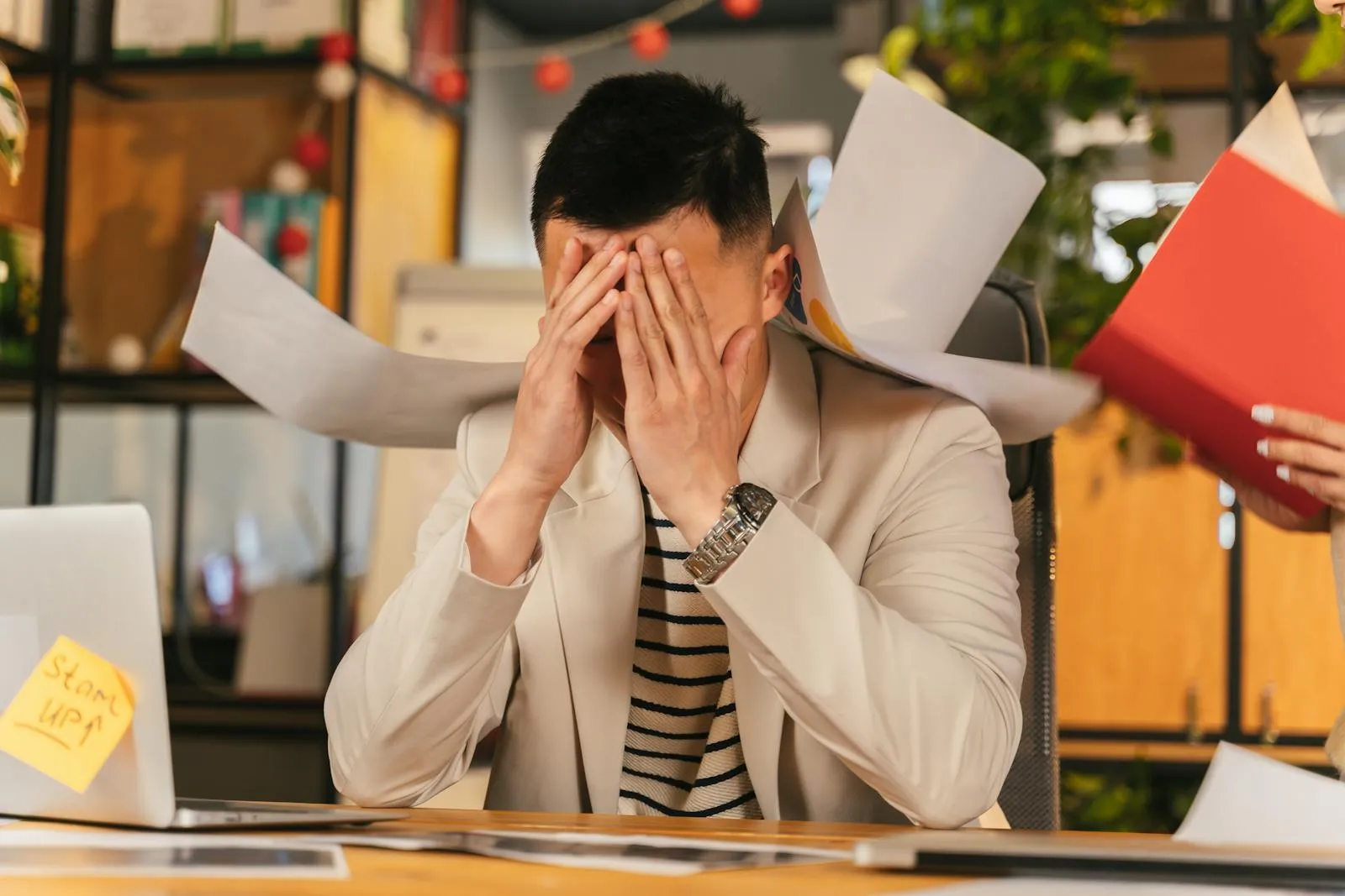 A businessman overwhelmed by paperwork at a cluttered office desk, showing visible signs of burnout