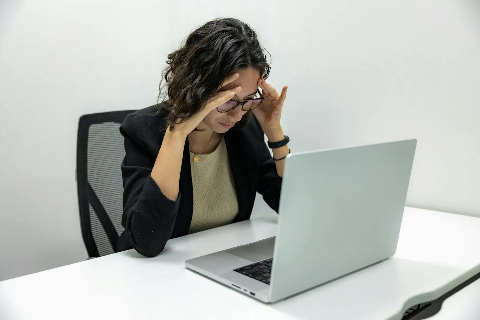 A young employee sits at a laptop holding her head, visibly burnt out from computer work